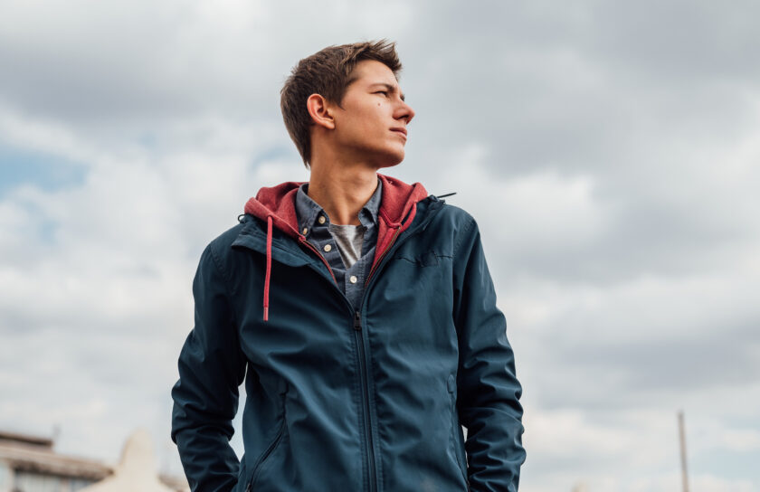 An urban young man in a blue jacket against a blue cloudy sky