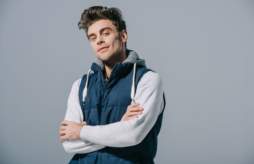 handsome fashionable man posing in waistcoat with crossed arms, isolated on grey